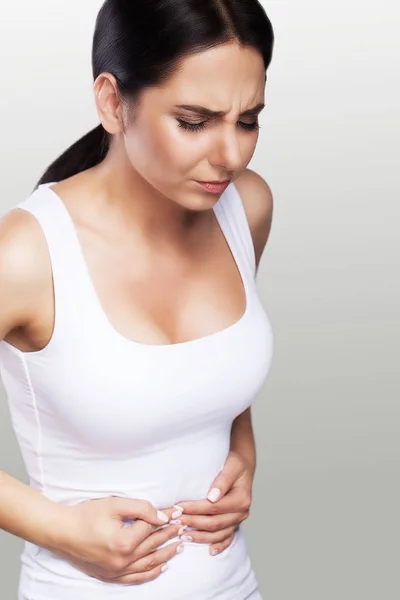 Dolor de estómago. Una joven siente dolor en el abdomen. Estómago. Dolor femenino. El concepto de salud. Sobre un fondo gris . — Foto de Stock