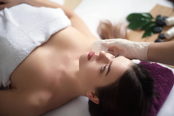 Bőr és testápolás. Közeli kép: egy fiatal nő egyre Spa kezelés szépségszalonban. Spa arc masszázs. Kezelése arc szépségét. Wellness szalon. — Stock Fotó