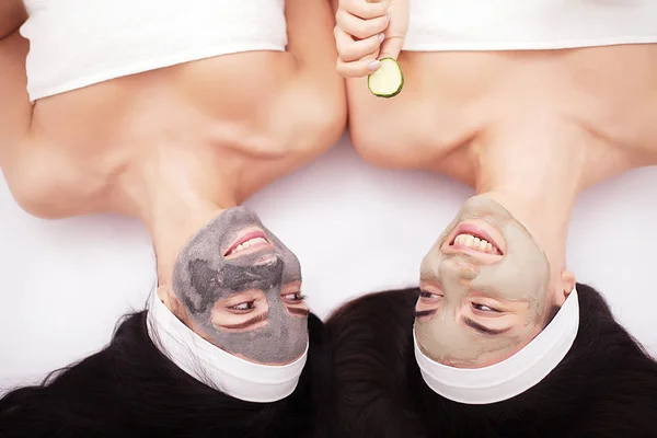 Home spa. Două femei tinere frumoase care țin bucăți de castravete pe ochi și zâmbesc în timp ce stau pe pat — Fotografie, imagine de stoc