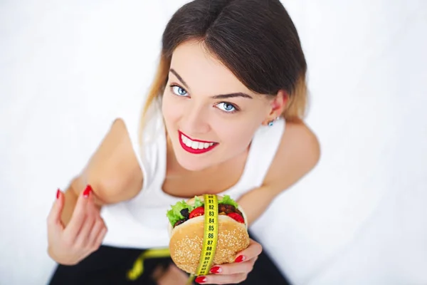 Diet. A young woman holding a burger in a measuring tape. A girl — Stock Photo, Image