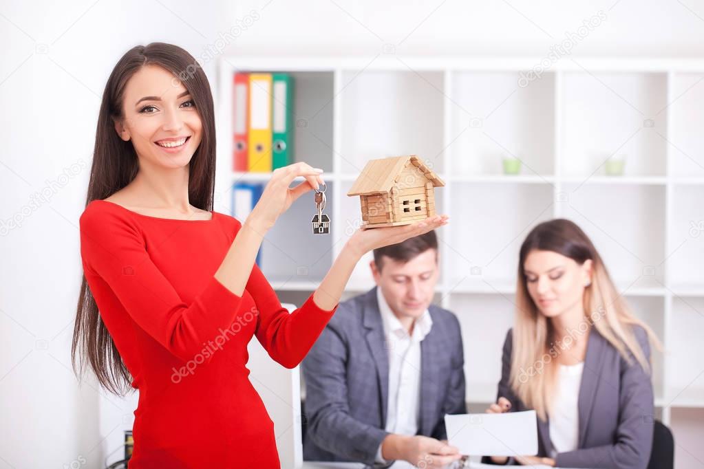 Cheerful realtor giving house key to happy property owners, youn