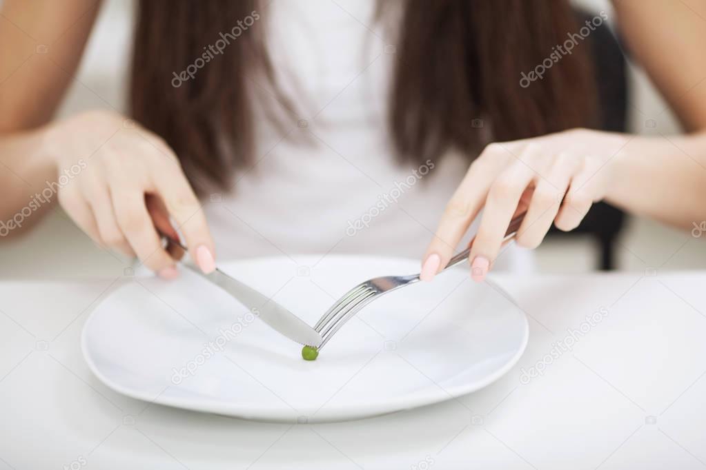 Eating disorder. Girl is holding a plate and trying to put a pea