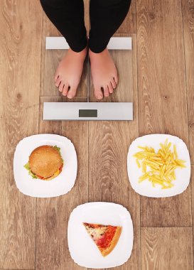 Güzel bir genç kadın üzerinde ölçekler olduğunu. Patates kızartması, pizza ve hamburger arasında seçim yapmak. Sağlıklı beslenme kavramı. Sağlıklı bir yaşam tarzı. Diyet.