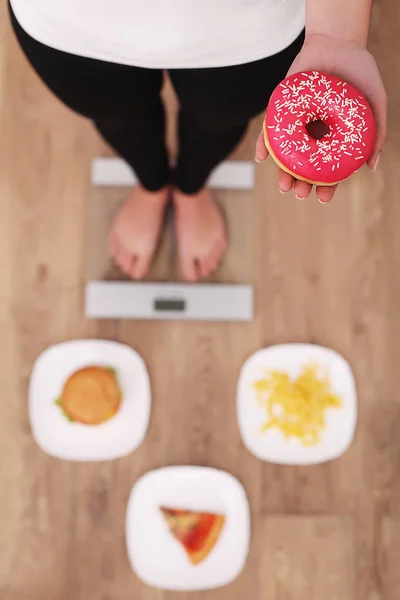 Jeune belle femme debout sur des écailles et tenant un beignet. Le concept de saine alimentation. Mode de vie sain. Régime alimentaire . — Photo