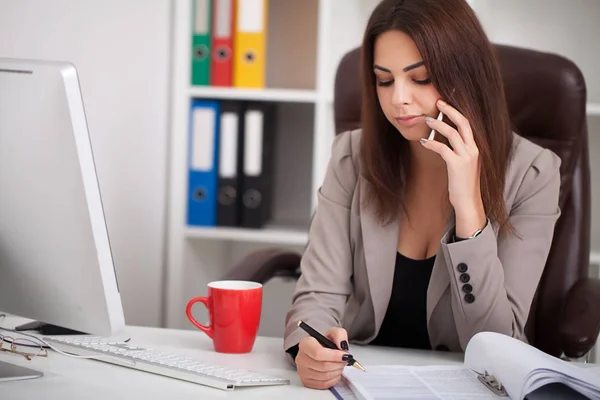 Young business woman working on laptop and talking on mobile pho — Stock Photo, Image