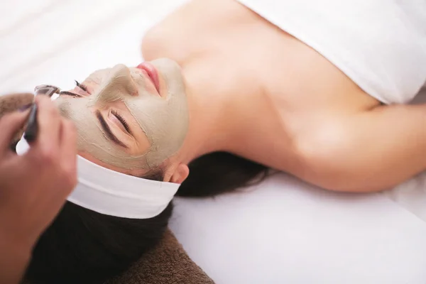 Hermosa joven mujer está recibiendo máscara de arcilla facial en el spa, mintiendo — Foto de Stock