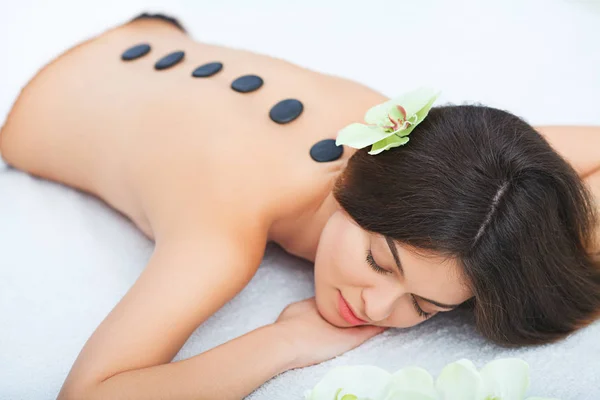 Schöne Frau entspannt sich im Wellness-Salon mit heißen Steinen am Körper. — Stockfoto