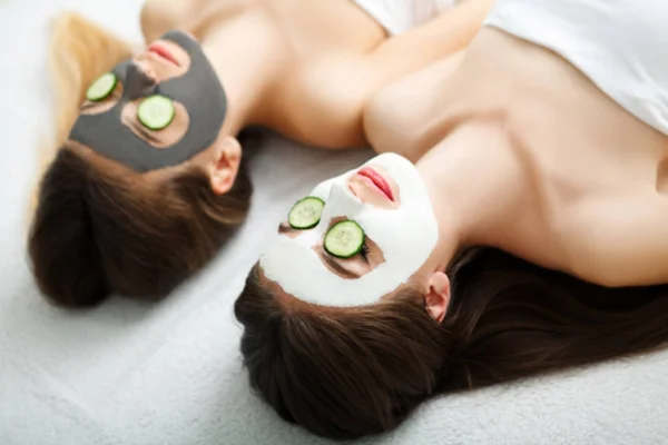 Spa en casa. Dos mujeres sosteniendo pedazos de pepino en sus rostros ly — Foto de Stock