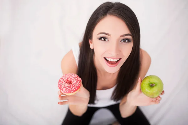 Concepto de dieta. Mujer joven eligiendo entre frutas y dulces —  Fotos de Stock