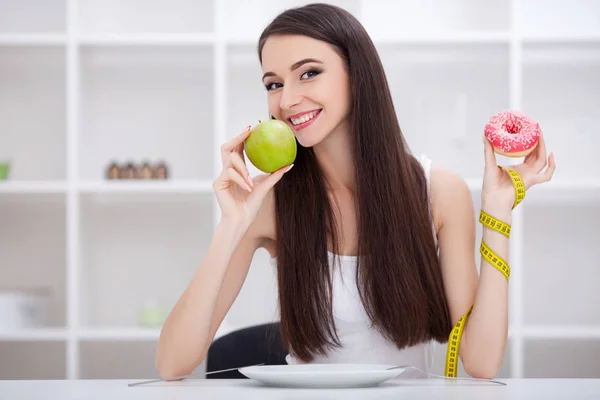 Dietkonceptet. Ung kvinna väljer mellan frukt och sötsaker — Stockfoto