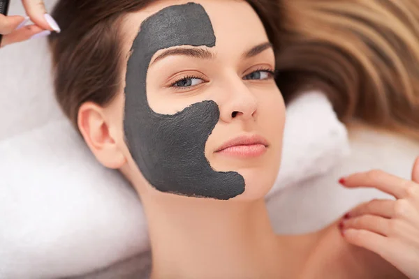 Spa. Atractiva mujer divertida con una máscara de barro en la cara. — Foto de Stock