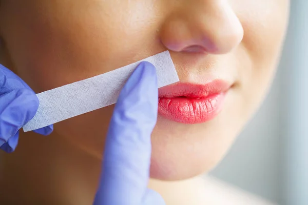 Beautician waxing young woman's eyebrows in spa center