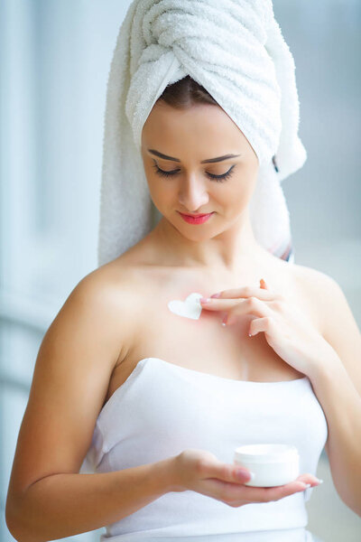 Studio shot of beautiful young woman applying moisturizer cream 