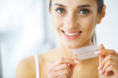 Diş beyazlatma. Şerit beyazlatma tutan güzel gülümseyen kadın