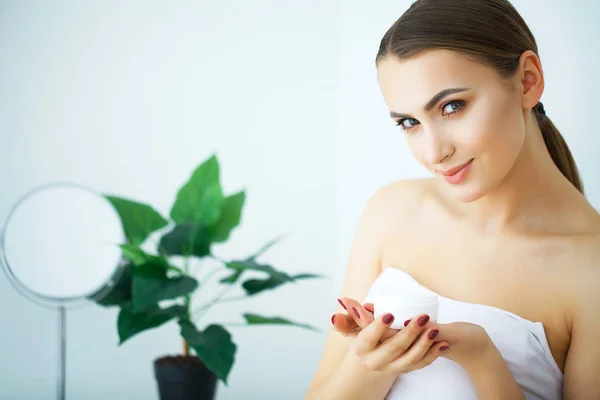 Una mujer hermosa usando un producto para el cuidado de la piel, crema hidratante o loti —  Fotos de Stock