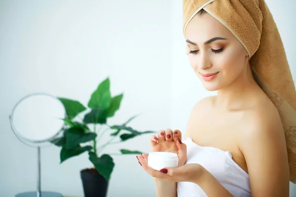 Una mujer hermosa usando un producto para el cuidado de la piel, crema hidratante o loti — Foto de Stock