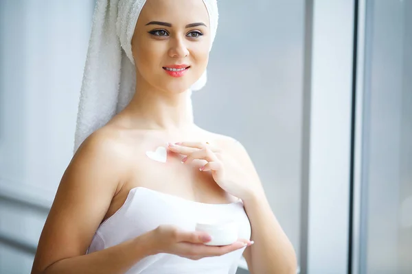 Mujer joven de pie en el baño y la aplicación de crema facial en el —  Fotos de Stock