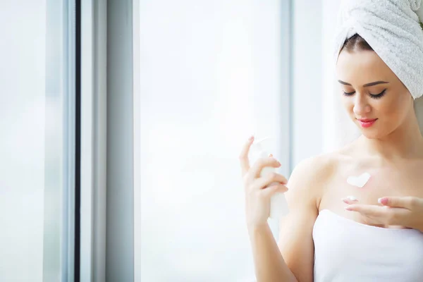 Mujer joven perfecta aplicando crema facial en el baño —  Fotos de Stock