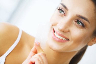 Diş beyazlatma. Şerit beyazlatma tutan güzel gülümseyen kadın