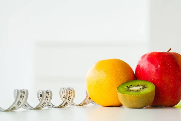Naranja, kiwi y manzana rodeados por una cinta métrica en bac blanco —  Fotos de Stock