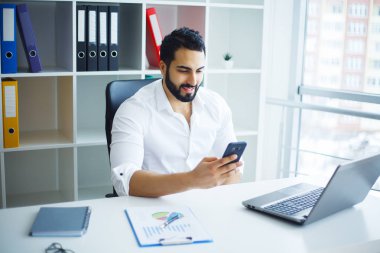 Ofisteki bilgisayarını kullanarak gülümseyen iş adamı.