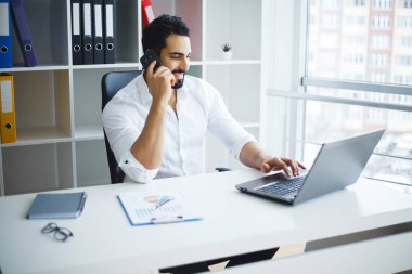 Ofisteki bilgisayarını kullanarak gülümseyen iş adamı.