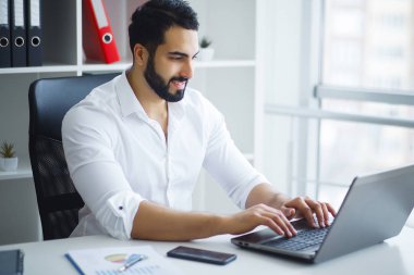 Ofisteki bilgisayarını kullanarak gülümseyen iş adamı.