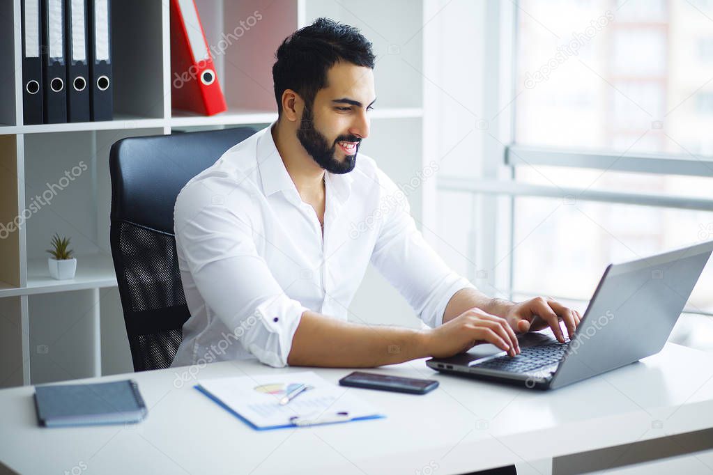 Smiling businessman using laptop at desk in office