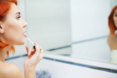 Banyoda kızıl saçlı bir kadın bakım ürünleri kullanıyor.