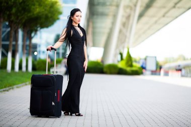 Tatil. Gülümseyen kadın yolcu havaalanı yolcu salonundan bavulçekerek kapıdan çıkışa doğru ilerliyor.