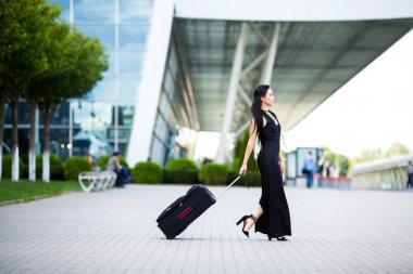 Tatil. Gülümseyen kadın yolcu havaalanı yolcu salonundan bavulçekerek kapıdan çıkışa doğru ilerliyor.