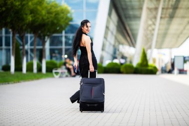 Tatil. Gülümseyen kadın yolcu havaalanı yolcu salonundan bavulçekerek kapıdan çıkışa doğru ilerliyor.