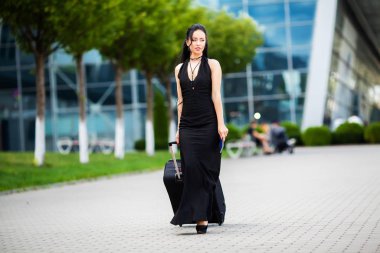 Tatil. Gülümseyen kadın yolcu havaalanı yolcu salonundan bavulçekerek kapıdan çıkışa doğru ilerliyor.