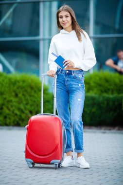 Tatil. Gülümseyen kadın yolcu havaalanı yolcu salonundan bavulçekerek kapıdan çıkışa doğru ilerliyor.