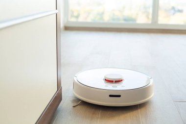 Akıllı Ev. Elektrikli süpürge robotu oturma odasında ahşap zeminde koşar.