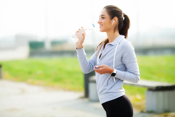 Hermosa mujer bebiendo agua y escuchar música después de correr — Foto de Stock