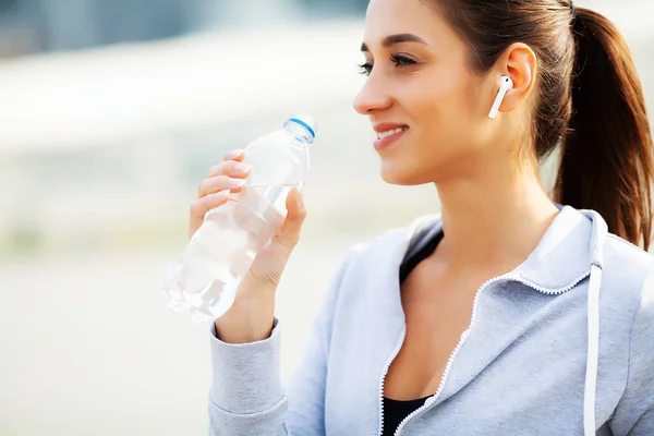 Красивая женщина пьет воду и слушает музыку после бега — стоковое фото