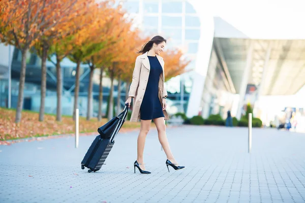 Smiling feminino passageiro processo para sair porta puxando mala através do aeroporto concurso . — Fotografia de Stock