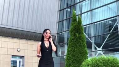 Havaalanındaki iş kadını havaalanında el bagajıyla yürürken akıllı telefondan konuşuyor. Sohbet için cep telefonu kullanan kız