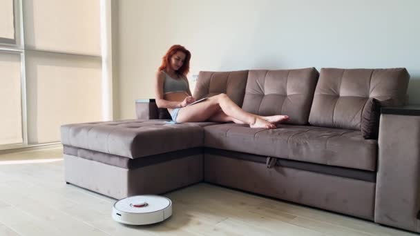 Inteligentny dom. Sprzątanie domów roboty odkurzacz, gdy kobiety na kanapie grać telefony komórkowe — Wideo stockowe