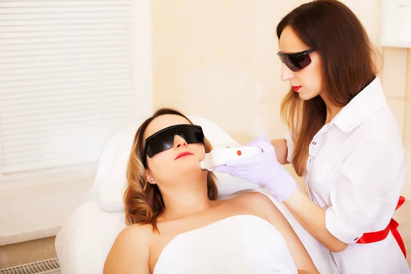 Esteticista dando tratamiento de la acumulación del laser a la cara joven de las mujeres en la clínica de la belleza . — Foto de Stock