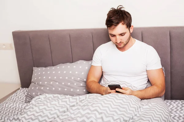 Hombre adicto a su teléfono móvil en la cama —  Fotos de Stock