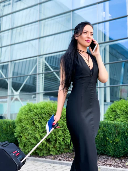 Business Woman in airport talking on the smartphone while walking with hand luggage in airport going to gate — Stock Photo, Image