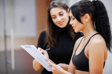 Female trainer teaching woman doing exercise in gym