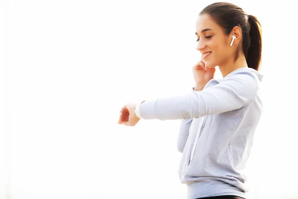 Φωτογραφία της γυναίκα χαρούμενη Fitness 30s Sportswear αγγίζοντας Bluetooth Earpod και κρατώντας το κινητό τηλέφωνο, ενώ αναπαύεται στο Green Park — Φωτογραφία Αρχείου