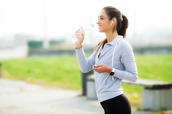 Όμορφη γυναίκα πίνει νερό και ακούει μουσική μετά το τρέξιμο — Φωτογραφία Αρχείου