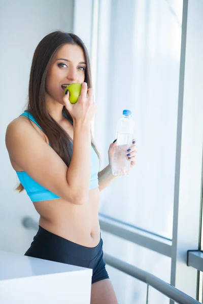 Молодая женщина держит в руках бутылку воды и зеленое яблоко — стоковое фото