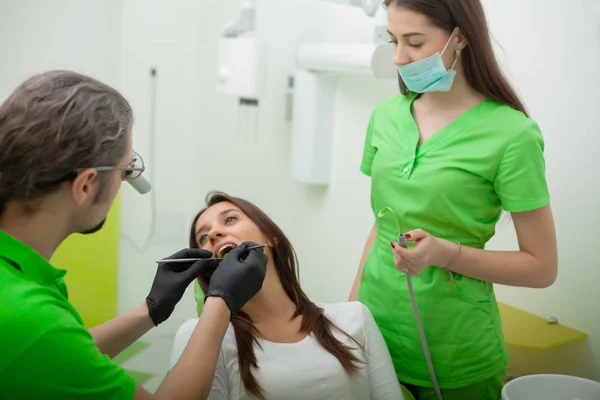 O dentista está a tratar dos dentes ao cliente no consultório dentário. — Fotografia de Stock