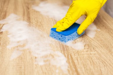 Çalışan ahşap masayı temizlemek için sünger kullanıyor.