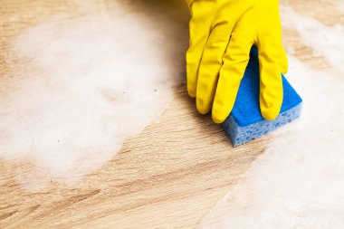 Çalışan ahşap masayı temizlemek için sünger kullanıyor.